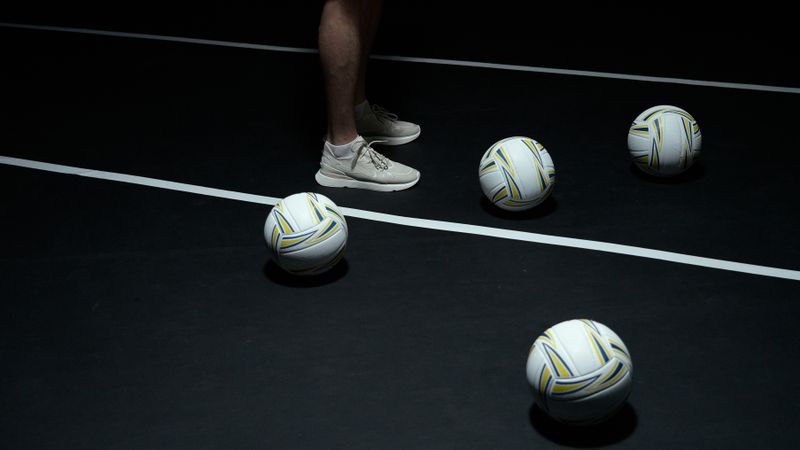 Volleyballs on a dark court floor beside athletic shoes, the mark for the gear desk.